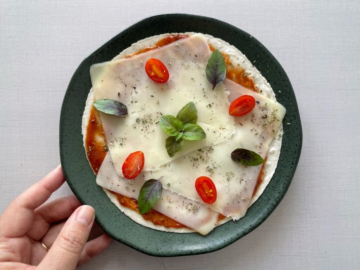 Pizza finalizada com tomate-cereja e mangericão.