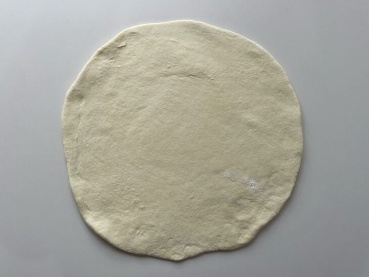 Massa crescida sobre a bancada polvilhada com farinha em formato circular.