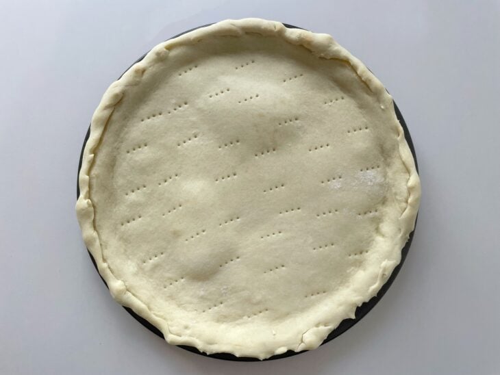 Garfo fazendo pequenos furos na superfície do disco de pizza aberto na assadeira.