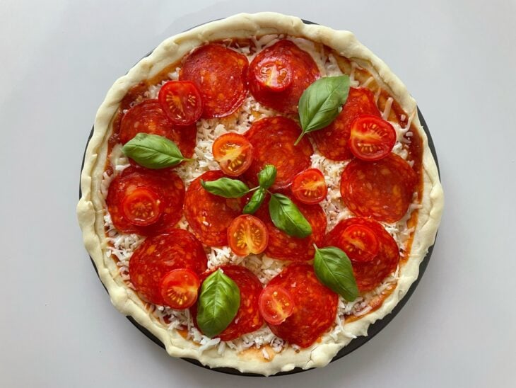 Metades de tomate-cereja e folhas verdes de manjericão sendo colocadas por cima do recheio.