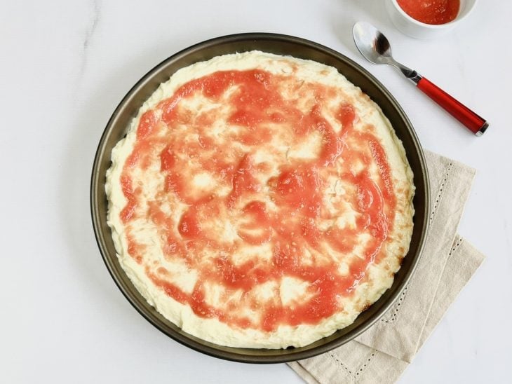 Uma assadeira com a massa de pizza e molho de tomate.