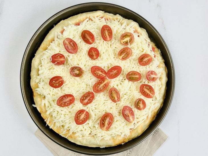 Uma assadeira com a massa de pizza, molho de tomate, queijo e tomate.