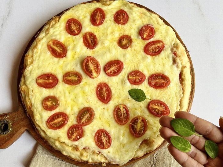Uma tábua com a pizza assada, com a adição de folhas de manjericão.