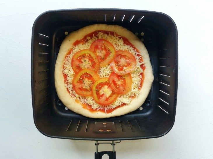 Uma cesta de airfryer contendo uma pizza recheada e crua.