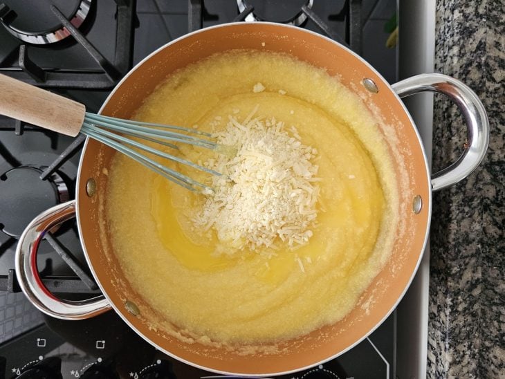 Uma panela cozinhando polenta e queijo ralado sendo adicionado.