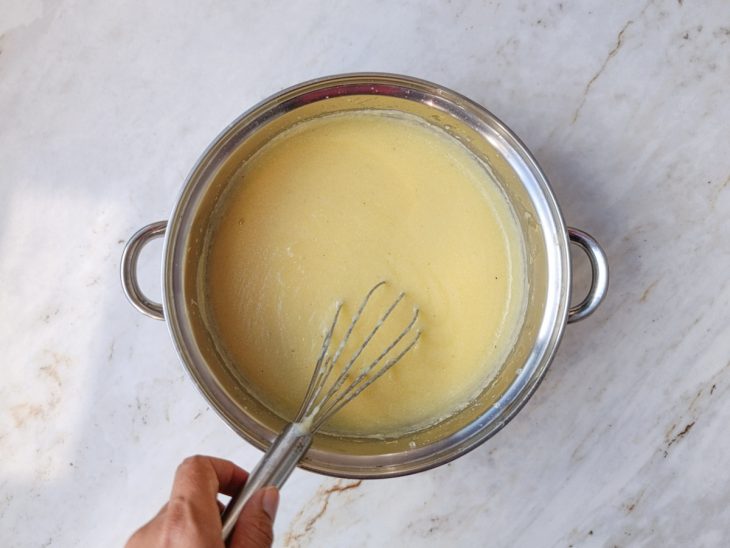 Conteúdo da panela temperado com sal e pimenta, sendo mexido por um fouet (batedor de arame).