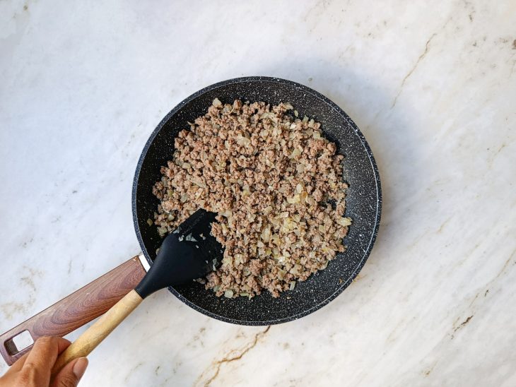 Carne moída refogada com cebola e alho numa frigideira.
