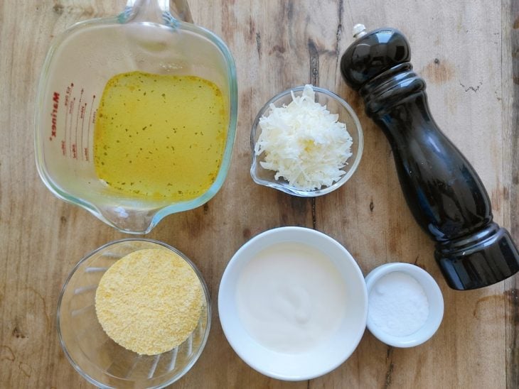 Ingredientes para a receita de polenta cremosa gratinada reunidos em uma superfície.