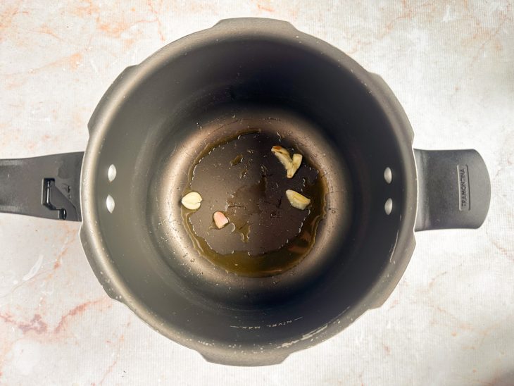 Alho dourando no azeite dentro da panela de pressão.