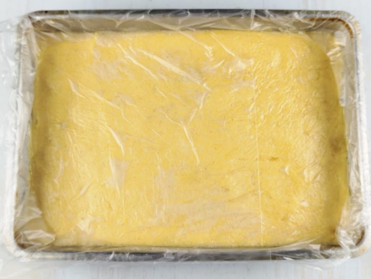 Polenta nivelada e assadeira coberta por plástico.