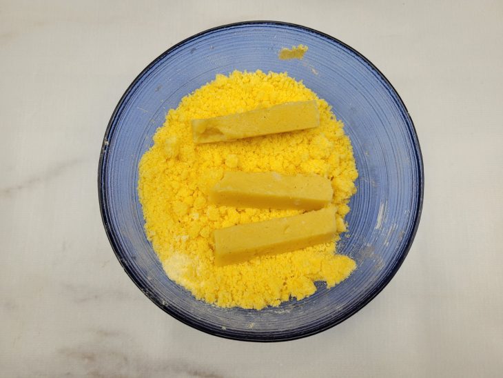 Palitos de polenta sendo empanados.