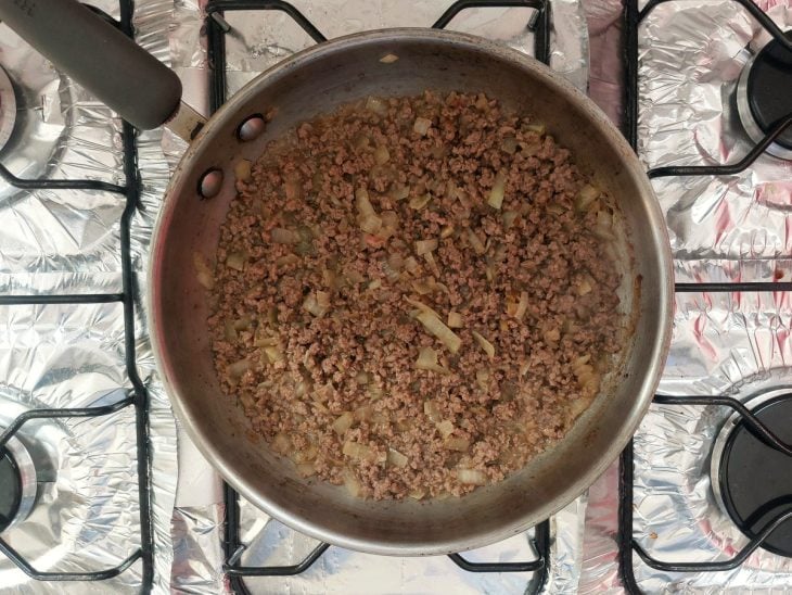 Uma panela com carne moída, cebola e caldo de carne.