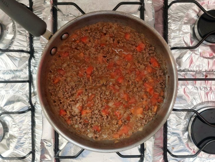 Uma panela com carne moída, cebola, caldo de carne e tomate.