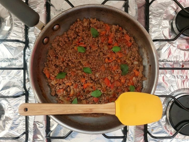Uma panela com carne moída, cebola, caldo de carne, tomate e manjericão.