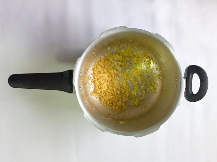 Alho e cebola dourados no azeite em uma panela de pressão.
