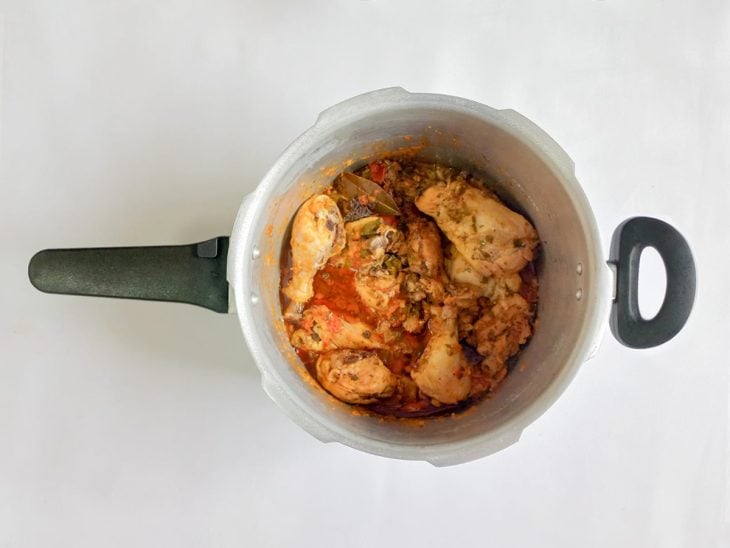 Frango, coentro e folhas de louro adicionadas na panela de pressão.