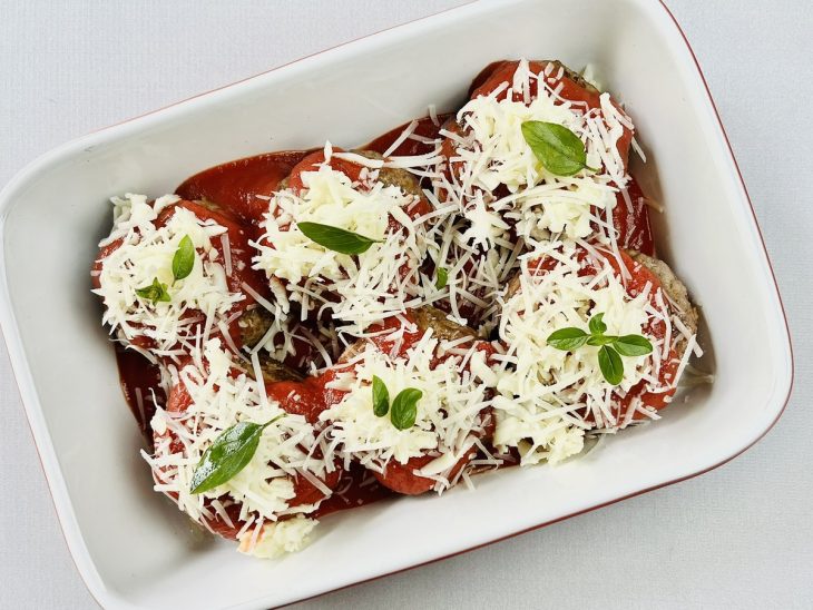 Polpetones cobertos com molho de tomate, folhas de manjericão e queijo mussarela ralado em um refratário.