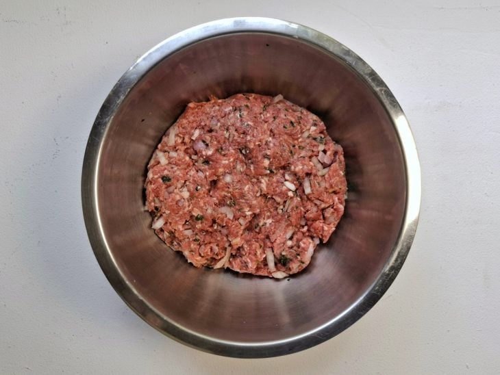 Carne moída e temperos adicionados em um recipiente.