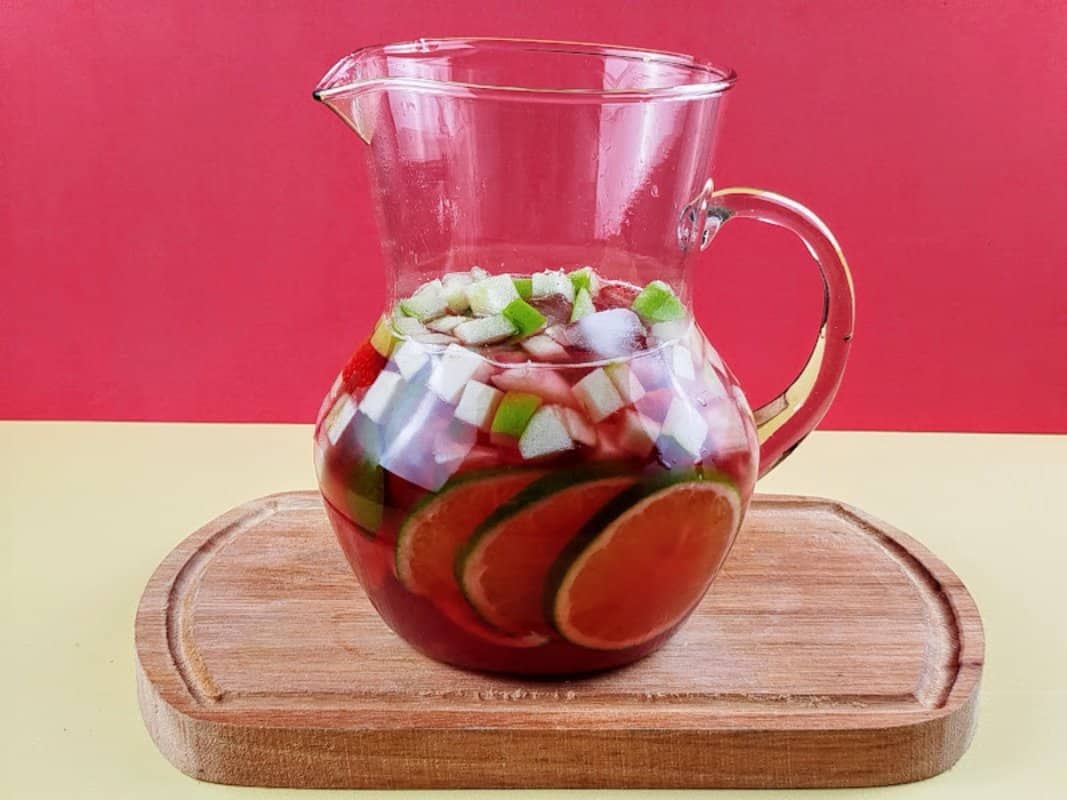 Jarra com chá gelado, frutas picadas, folhas de hortelã e gelo.