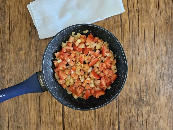 Uma frigideira refogando a cebola, o alho e o tomate.