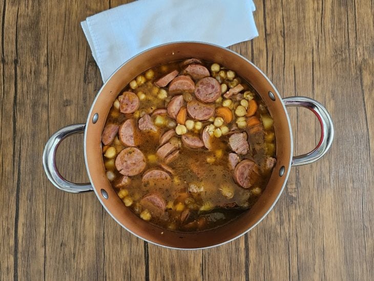 Uma panela cozinhando legumes e carnes, com o grão-de-bico.