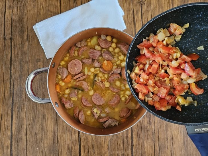 Uma panela cozinhando legumes e carnes, com o grão-de-bico e os refogados.