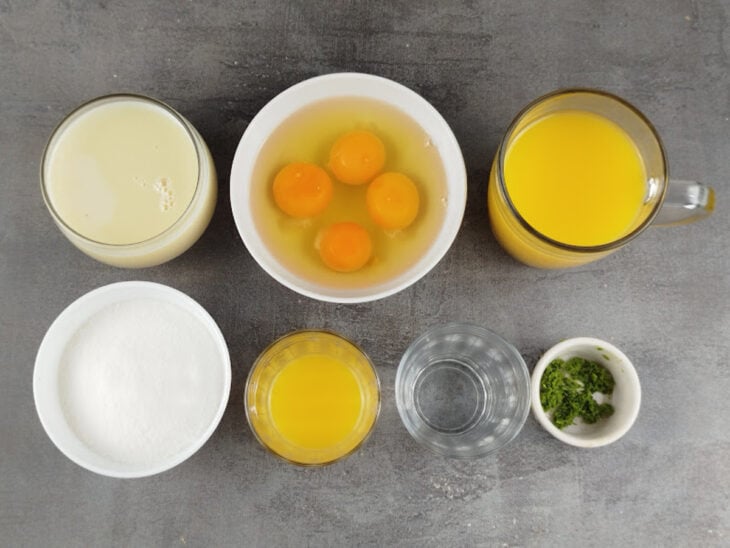 Ingredientes do pudim e da calda organizados na bancada com laranjas, ovos e leite condensado.