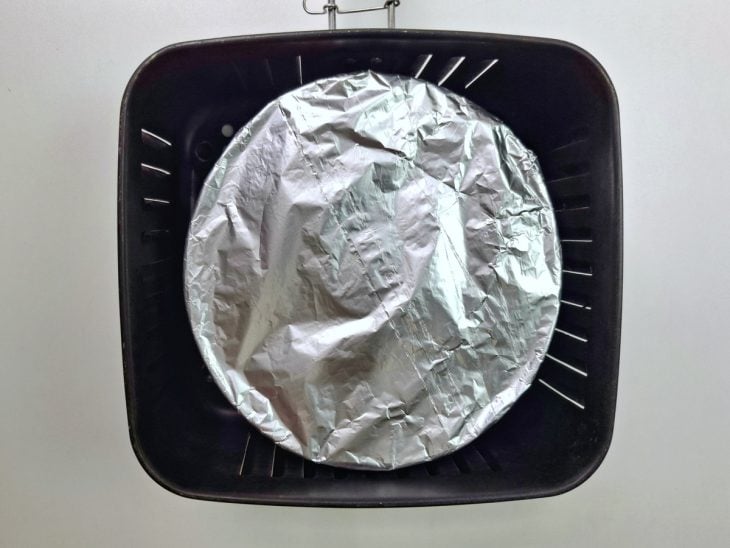Forma de pudim coberta com papel-alumínio dentro do cesto da air fryer.