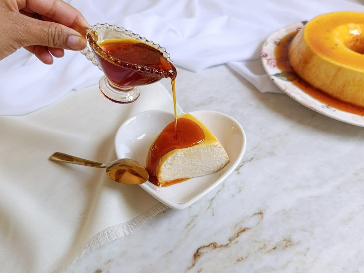 Calda sendo despejada sobre uma fatia do pudim.