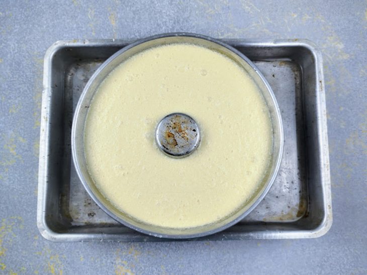 Uma assadeira com água contendo a forma com pudim para assar em banho-maria.