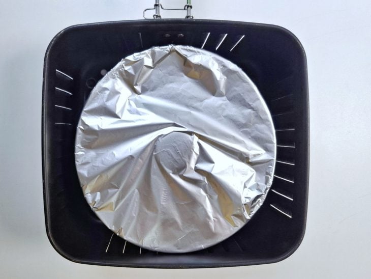 Forma de pudim coberta com papel-alumínio dentro do cesto da airfryer.