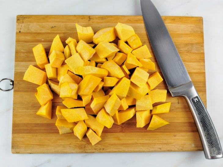 Abóbora descascada e cortada em cubinhos sobre uma tábua de cozinha.