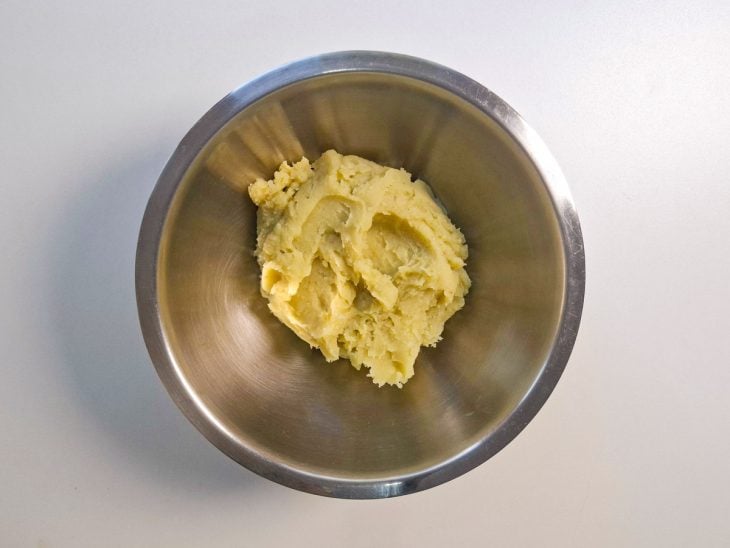 Batata-doce cozida sendo amassada com garfo em uma tigela.