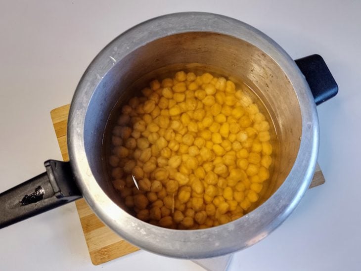 Uma panela de pressão contendo grão-de-bico coberto com água.