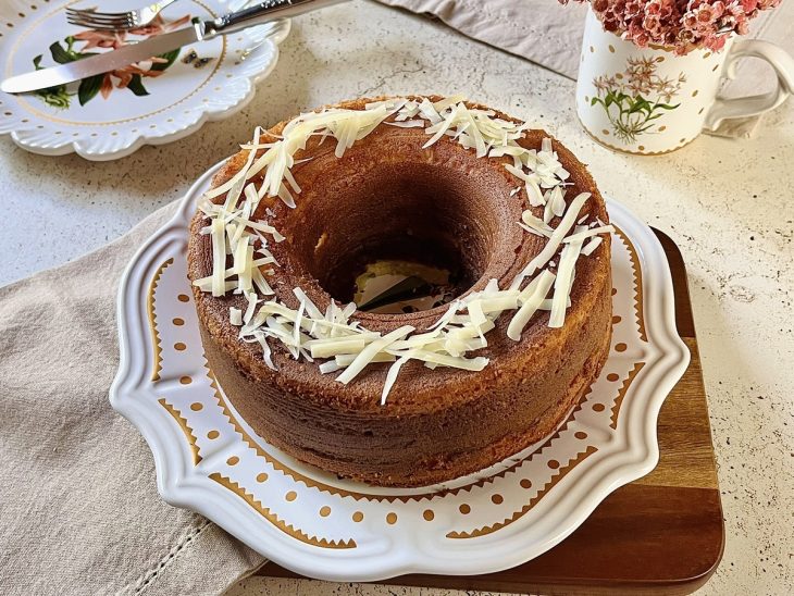 Queijadinha desenformada em um prato e finalizada com queijo parmesão ralado.