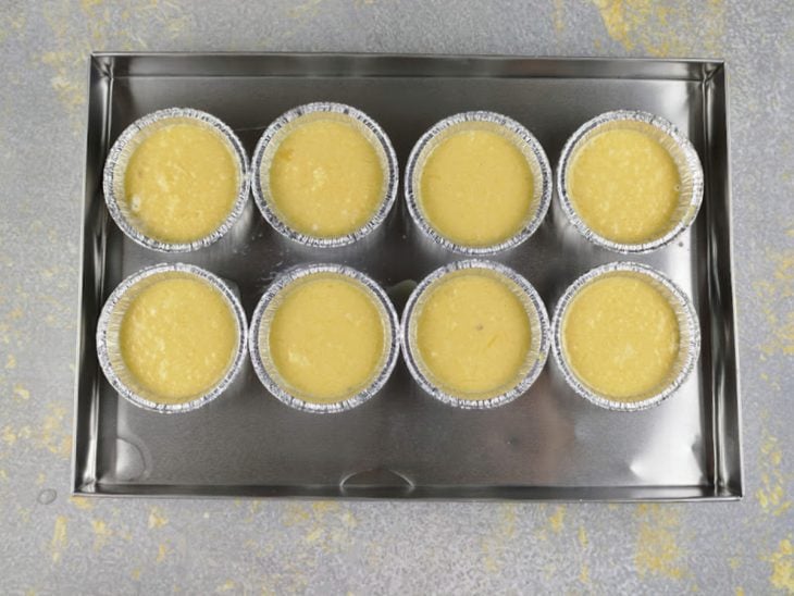Queijadinhas em forminhas de alumínio sobre uma assadeira com água quente.