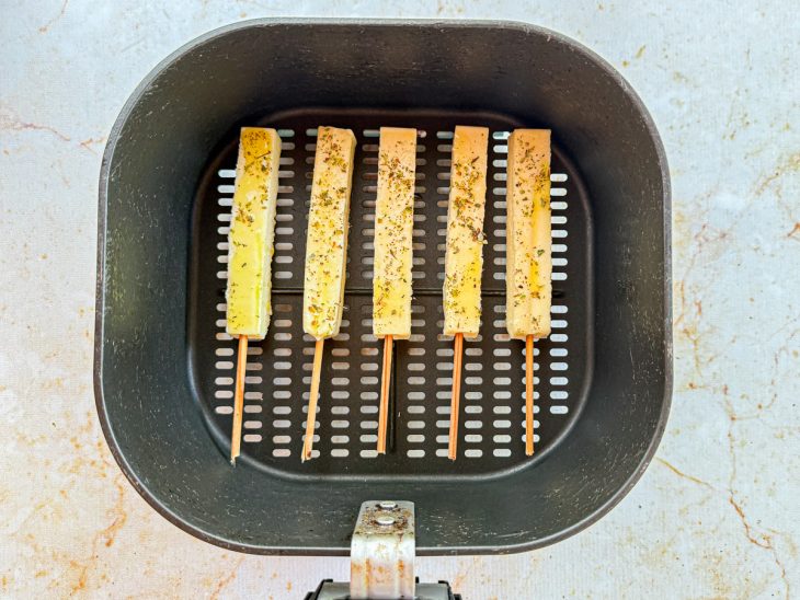 Espetos sendo dispostos na cesta da air fryer com espaço entre eles.