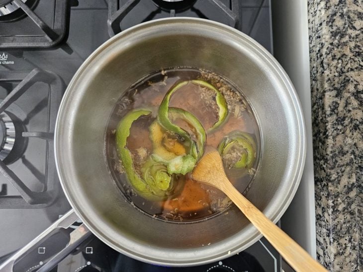 Panela com caramelo derretido na água, cascas das frutas e especiarias.