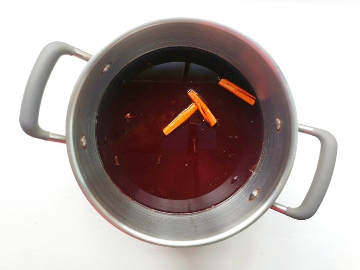 Panela de ferro com mistura em cor avermelhada com canelas em pau boiando.