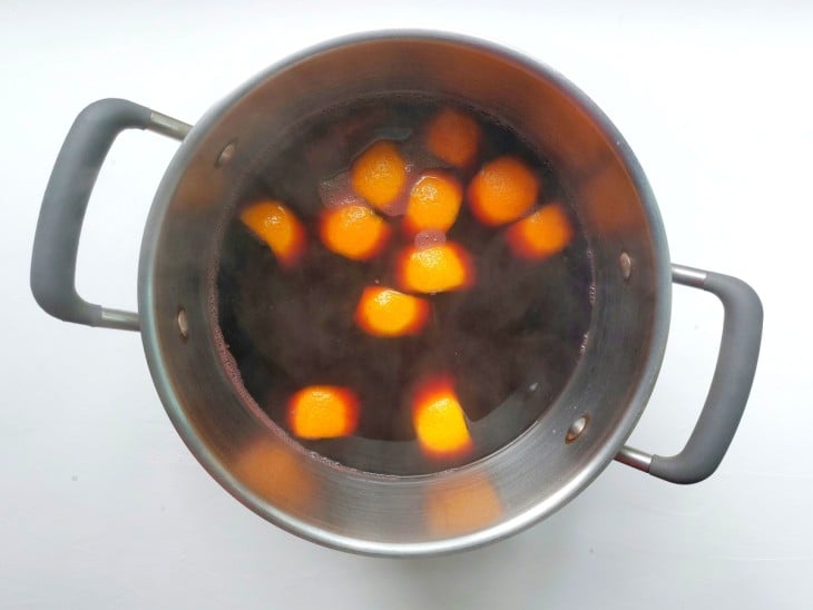 Panela de ferro com mistura em cor avermelhada com cascas de laranja boiando.