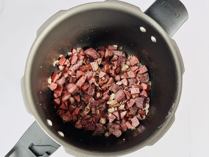 Bacon, charque e calabresa adicionados em uma panela.