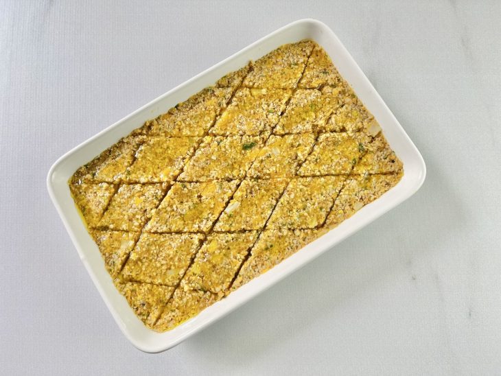 Massa do quibe sendo espalhada e nivelada na travessa.