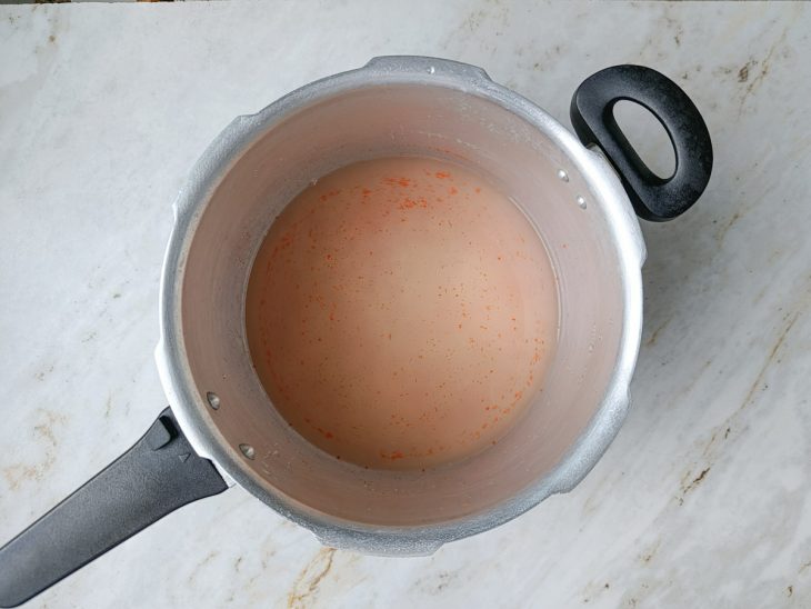 Arroz, água, colorau e sal colocados na panela de pressão.