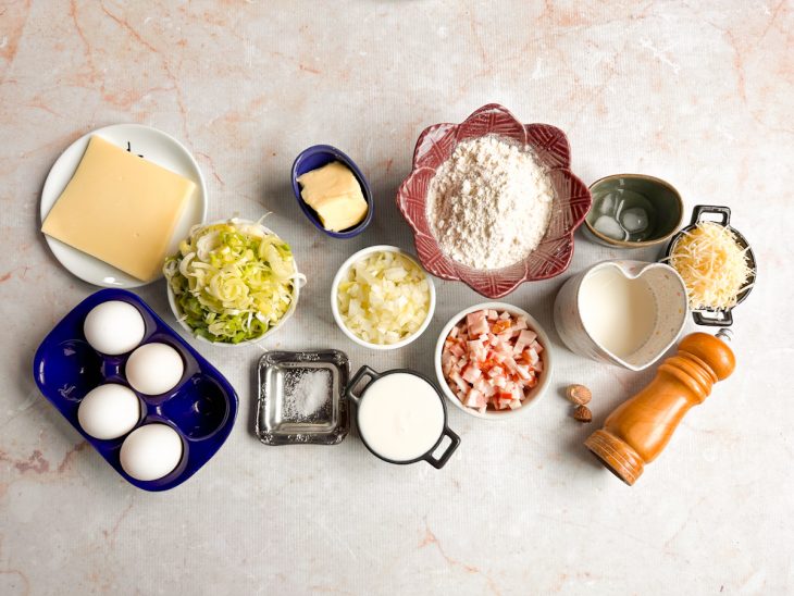 Ingredientes organizados na bancada com bacon, alho-poró e ovos picados.