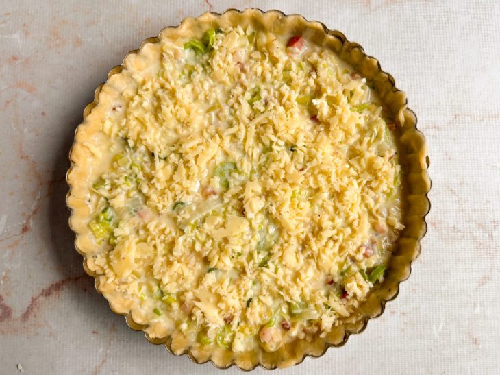 Recheio distribuído sobre a massa com cobertura de mussarela ralada.