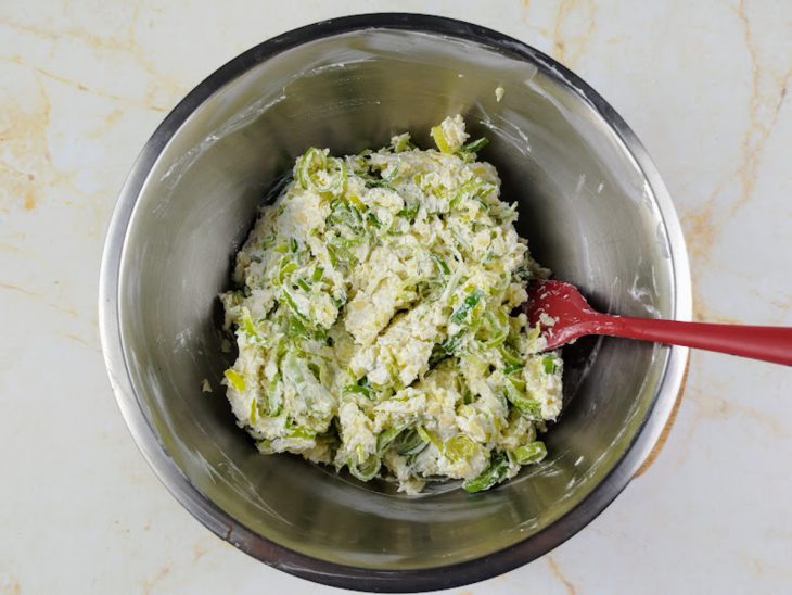 Mussarela ralada, alho poró, azeite, sal e cream cheese misturados em uma tigela.