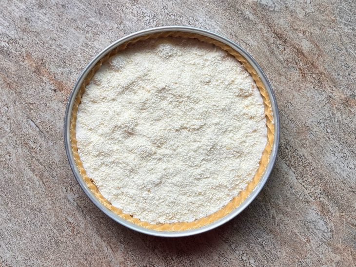 Camadas de queijo gouda ralado, mistura da batedeira e queijo parmesão ralado adicionadas na forma forrada com a massa.