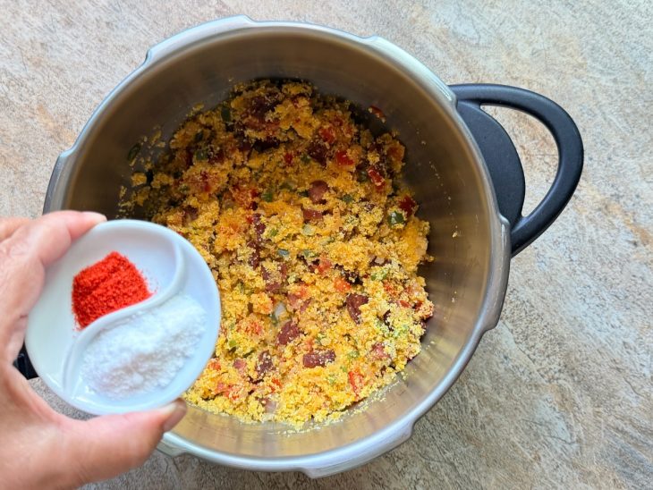 Na panela, colorau e sal sendo adicionados.