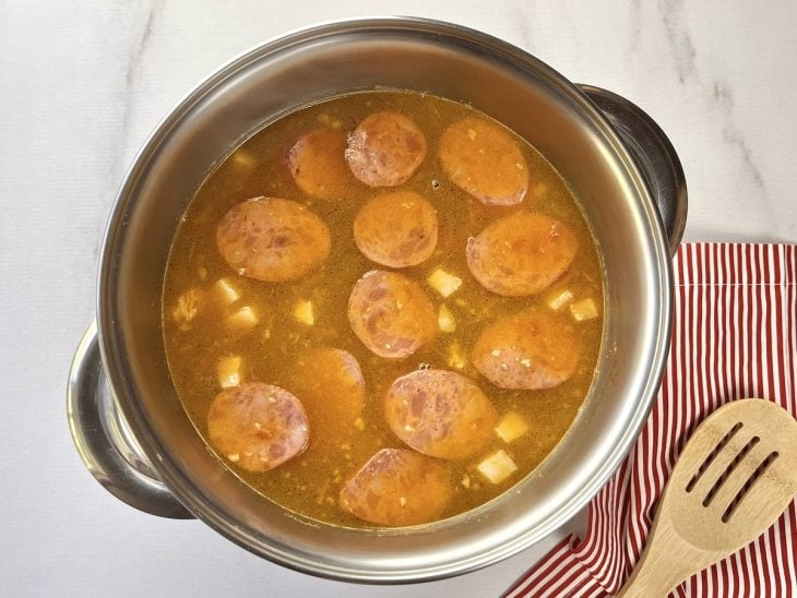 Uma panela com carne de porco, calabresa, água e temperos cozinhando.