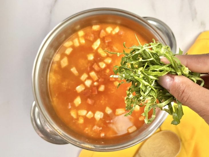 Uma panela com as costelinhas, bacon, calabresa, quirera, água, couve e temperos.
